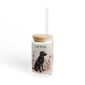 May include: A clear glass can with a bamboo lid and a straw. The can has a floral design with a black Labrador Retriever sitting in the center. The text "LAB MOM" is printed on the can.