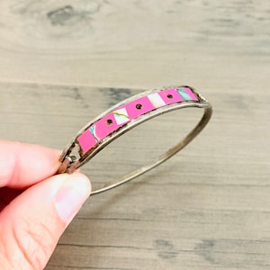 May include: A silver bangle bracelet with a pink and white inlay design. The inlay is made of small squares and circles.