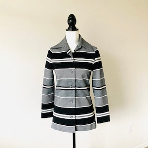 May include: A black and white striped long-sleeved shirt with a button-up front. The shirt has a collar and is made of a knit fabric.