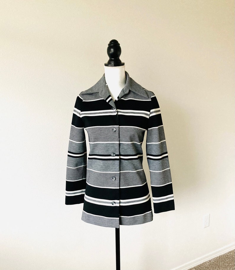 May include: A black and white striped long-sleeved shirt with a button-up front. The shirt has a collar and is made of a knit fabric.