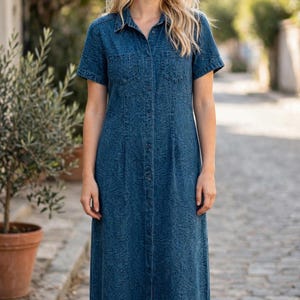 May include: A dark blue denim shirt dress featuring a subtle tonal leaf pattern, a classic collar, short sleeves, and a full-length button-down front. The garment includes two chest pockets and side slits at the hem, providing a structured silhouette.