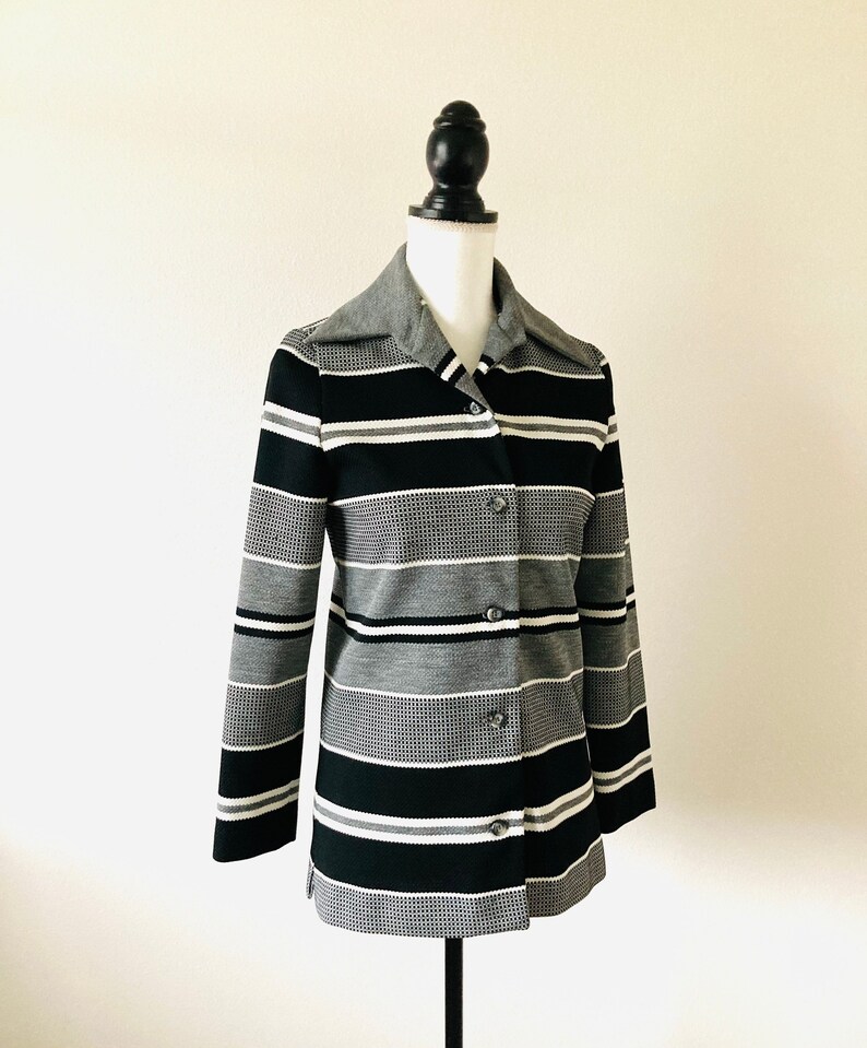 May include: A black, white, and gray striped button-up jacket with a collar.