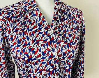 May include: A long-sleeved button-up shirt with a white background and a pattern of red and blue abstract shapes.