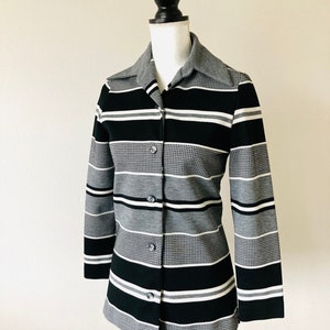 May include: A black and white striped button-up shirt with a gray collar. The shirt is made of a textured fabric and has long sleeves.