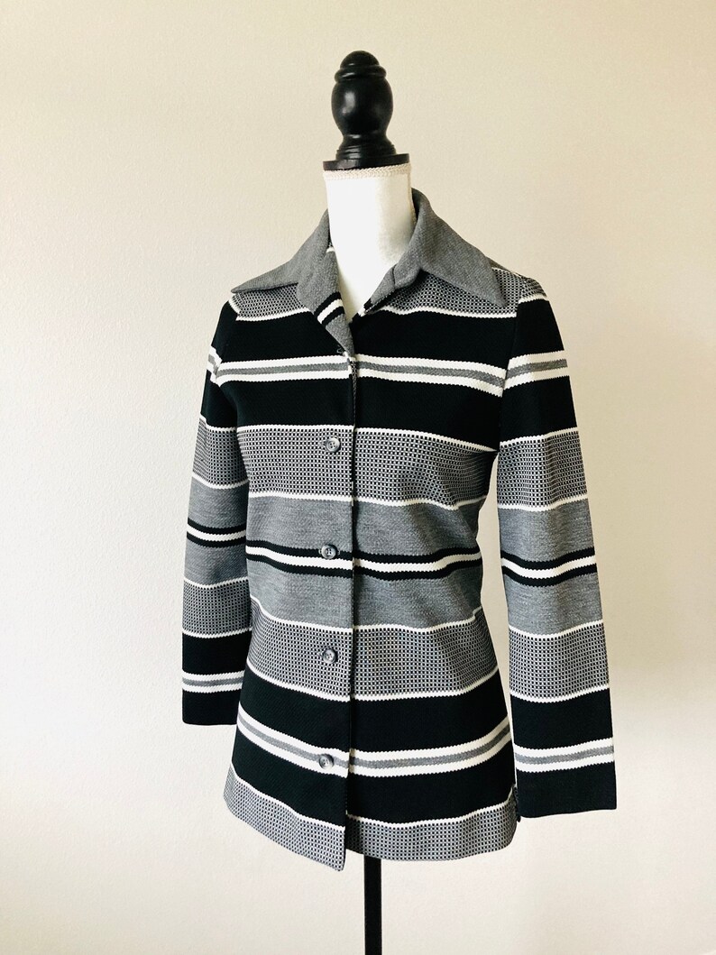 May include: A black and white striped button-up shirt with a gray collar. The shirt is made of a textured fabric and has long sleeves.