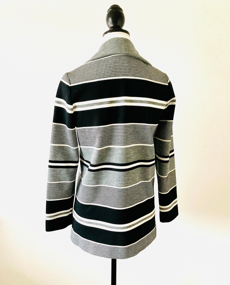 May include: A black and white striped blazer with a textured pattern. The blazer has a collar and long sleeves.