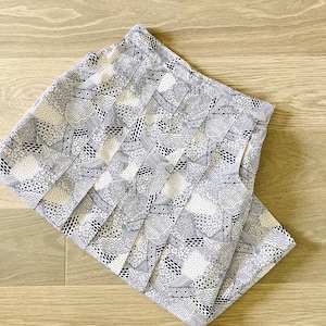 May include: Folded white and navy blue patterned fabric. The fabric features a repeating design of geometric shapes, including dots, lines, and curves. The fabric is lying on a light brown wooden surface.