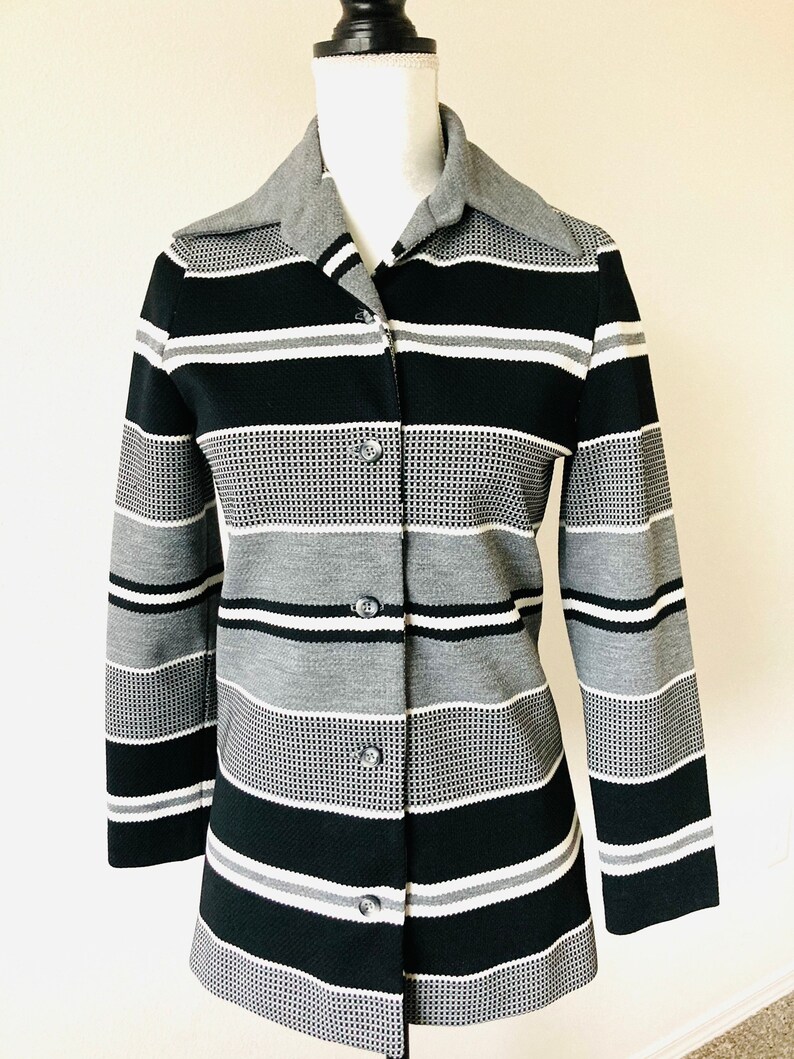 May include: A long-sleeved button-up shirt with a striped pattern in black, white, and gray. The shirt has a collar and a button-up front.