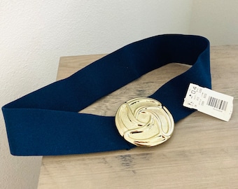 May include: A dark blue elastic belt with a large gold-toned buckle featuring a swirling design. The buckle is round and has a textured surface.
