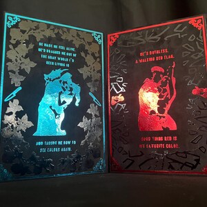 May include: Two framed art pieces with black backgrounds. One features a blue silhouette with text: "He made me feel alive...and taught me how to see colors again." The other has a red silhouette and text: "He's ruthless...good thing red is my favorite color."