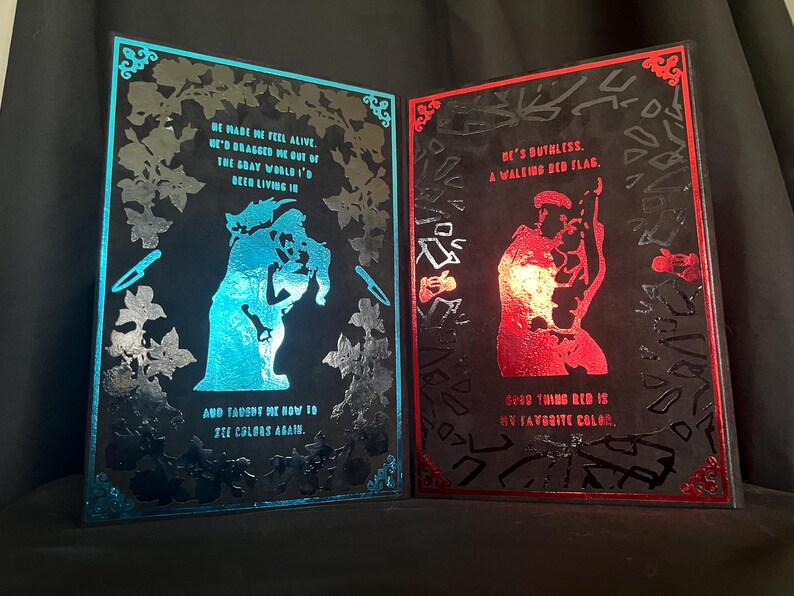 May include: Two framed art pieces with black backgrounds. One features a blue silhouette with text: "He made me feel alive...and taught me how to see colors again." The other has a red silhouette and text: "He's ruthless...good thing red is my favorite color."