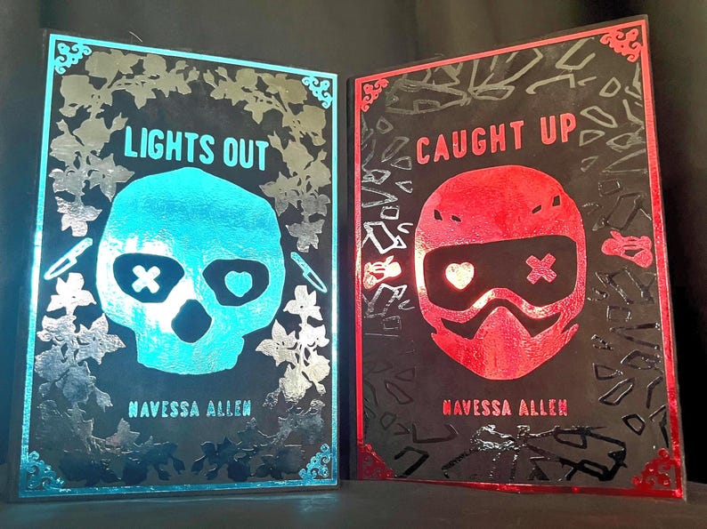 May include: Two illuminated art pieces with black backgrounds. One features a blue skull with the text "LIGHTS OUT" and the author's name. The other has a red helmet design with the text "CAUGHT UP" and the author's name. Both have floral and geometric accents.