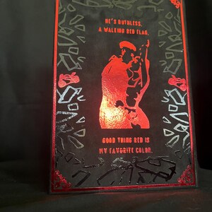 May include: A black rectangular art print with red accents and text. The print features a red silhouette of a person and the phrases "HE'S RUTHLESS. A WALKING RED FLAG. GOOD THING RED IS MY FAVORITE COLOR."