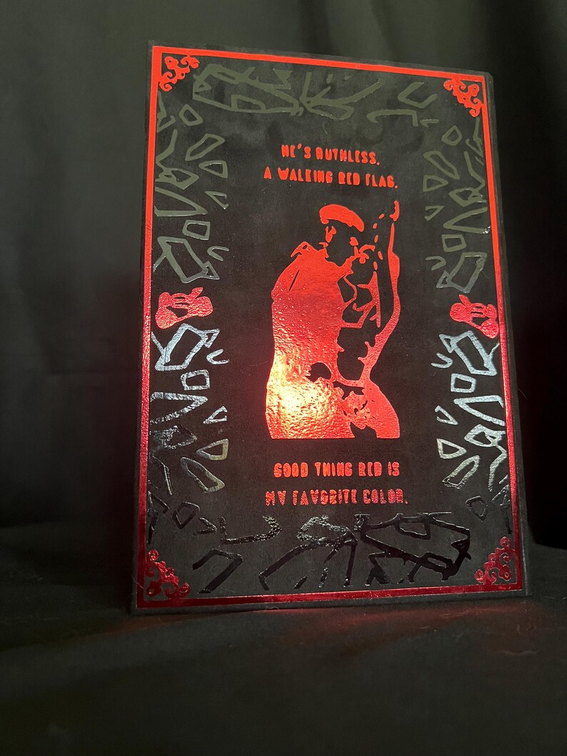 May include: A black rectangular art print with red accents and text. The print features a red silhouette of a person and the phrases "HE'S RUTHLESS. A WALKING RED FLAG. GOOD THING RED IS MY FAVORITE COLOR."