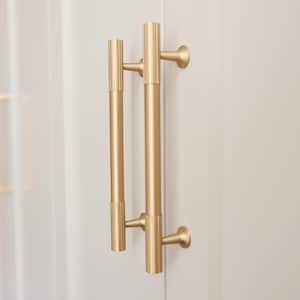 May include: Close-up of two gold door handles. The cylindrical handles have a ribbed texture on the ends and are mounted on a white door. The handles have a modern, minimalist design.