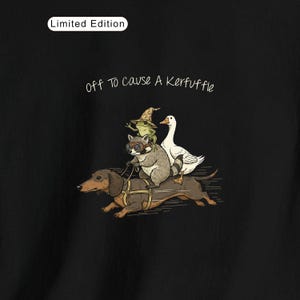 Könnte beinhalten: Schwarzes Grafik-T-Shirt mit dem Text "Off to Cause a Kerfuffle". Das Design zeigt einen Dackel, der einen Waschbären mit Brille, einen Frosch mit Hexenhut und eine Gans zieht. Oben steht "Limited Edition".