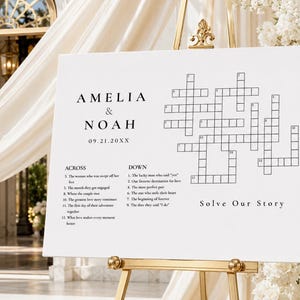 Könnte beinhalten: Ein weißes Schild mit einem Kreuzworträtsel, das auf einer goldenen Staffelei ausgestellt ist. Das Schild zeigt die Namen "Amelia & Noah" und das Datum "09.21.20XX". Das Kreuzworträtsel enthält Hinweise, die sich auf die Geschichte eines Paares beziehen, mit dem Satz "Solve Our Story" unten.