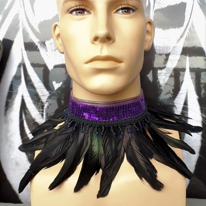 May include: A decorative collar with a purple sequin band and black feather design. The collar is decorated with small blue beads and is displayed on a mannequin.