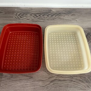 Op de afbeelding: Twee rechthoekige plastic opbergbakjes, één in een dieprode kleur en de andere in een lichte crèmekleur. Beide bakjes hebben een getextureerde bodem met een raster van kleine, verhoogde piramidevormige bultjes aan de binnenkant.
