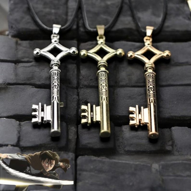 May include: Three key-shaped pendants on black cords. The keys are silver, gold, and bronze, each with a diamond-shaped top and detailed inscriptions. The background is a dark, textured surface.