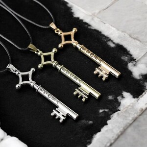 May include: Three metal key pendants on black cords. The keys are in gold, silver, and bronze tones, each with a decorative handle and a key shaft with Japanese characters. The keys are displayed on a dark surface.