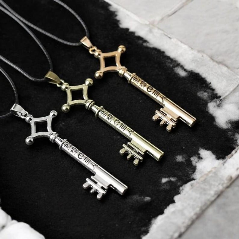 May include: Three metal key pendants on black cords. The keys are in gold, silver, and bronze tones, each with a decorative handle and a key shaft with Japanese characters. The keys are displayed on a dark surface.
