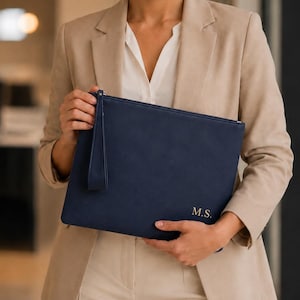 May include: A navy blue rectangular zippered clutch bag with a wrist strap. The bag features the gold-colored monogram initials M.S. embossed in the bottom right corner. The clutch has a smooth, matte finish and a simple, functional design.