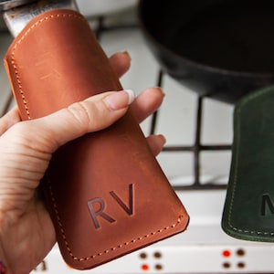 May include: Two leather pot holders with initials, one brown with "RV" and one green with "MU".
