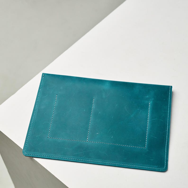 May include: Teal leather envelope clutch with stitched detailing.