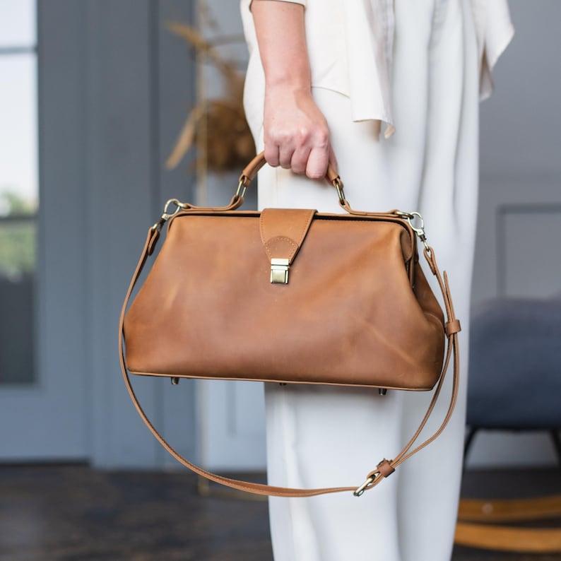 Elevate your style with this handmade leather doctor bag for women, crafted from premium leather for durability and elegance. Featuring a vintage-inspired design, a spacious interior, and an adjustable crossbody strap, it’s both stylish and practical. Customize it with personalized engraving for a unique touch. Order now and carry timeless sophistication every day!