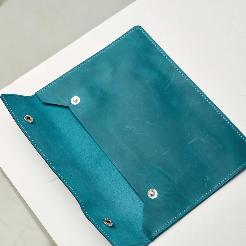 May include: A teal leather folder with a flap closure and metal poppers. The folder is open and the inside is visible.