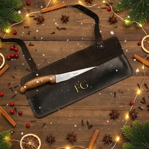 May include: A brown-handled knife in a black leather sheath, with the initials "FG" in gold. The knife is partially visible, set against a festive backdrop with cinnamon sticks, star anise, and evergreen sprigs.