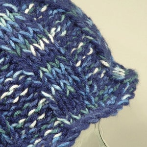May include: A blue, white, and green knitted beanie hat with a cable knit pattern.