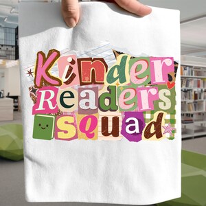 Puede incluir: Bolso tote blanco con el texto "Kinder Readers Squad" en un diseño colorido estilo collage. El texto está compuesto por varias fuentes y colores, incluyendo rosa, verde y marrón, creando una estética lúdica. El bolso es sostenido por una mano.
