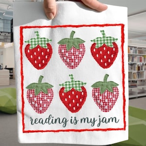 Puede incluir: Bolsa de mano blanca con seis fresas bordadas en rojo y blanco, con hojas verdes a cuadros. El texto "reading is my jam" está bordado en negro, dentro de un borde rojo cosido.