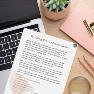 May include: A close-up of a wedding venue questionnaire booklet with a laptop, pencils, a magnifying glass, and a small potted succulent plant on a wooden table. The questionnaire is titled "Wedding Venue Questionnaire" and includes a list of topics to consider when choosing a venue.
