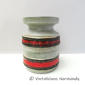 Peut inclure: Un vase en céramique gris avec des rayures rouges et noires. Le vase a une surface texturée et un sommet légèrement évasé.