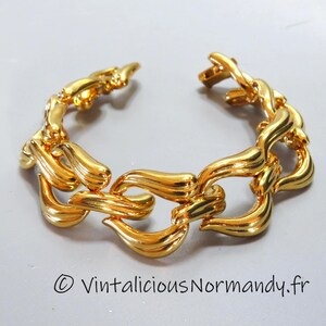 Op de afbeelding: Een goudkleurige armband met een uniek schakelontwerp. De schakels zijn gebogen en getextureerd, wat een elegant en opvallend accessoire creëert. De armband is open, wat het ontwerp laat zien. De algehele esthetiek is vintage en luxueus.