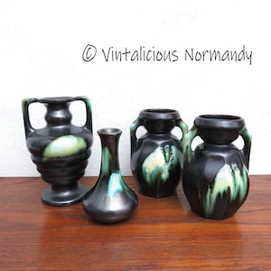 Peut inclure: Quatre vases en céramique de couleur noire, verte et blanche. Les vases sont de tailles et de formes différentes, deux d'entre eux ayant des anses. Les vases sont posés sur une surface en bois.