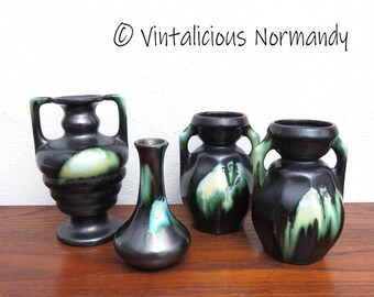 Pode incluir: Quatro vasos de cerâmica em esmalte preto, verde e branco. Os vasos são de diferentes tamanhos e formas, dois deles com alças. Os vasos estão sobre uma superfície de madeira.