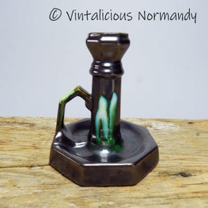 Peut inclure: Un bougeoir en céramique noire avec un glaçage vert et blanc. Le bougeoir a une poignée et une base ronde.