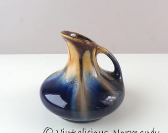 Pode incluir: Jarro de cerâmica com formato único e alça. O jarro apresenta uma base azul escuro que transita para um topo marrom dourado e bege. Possui acabamento brilhante e um bico curvo.