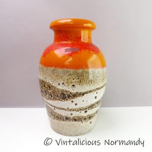 May include: A vintage ceramic vase with a glossy orange top and a textured, speckled body. The vase features a band of red and orange, transitioning to a white and brown pattern. The vase has a cylindrical shape with a slightly flared top.