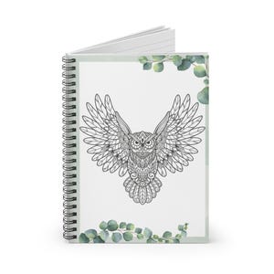 Könnte beinhalten: Ein spiralgebundenes Notizbuch mit weißem Hintergrund und einer Schwarzweißillustration einer Eule mit ausgebreiteten Flügeln. Die Eule ist von grünen Aquarellblättern umgeben.