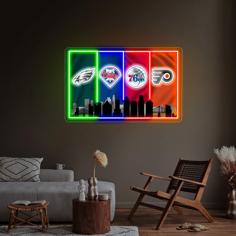 May include: A rectangular neon wall sign featuring four vertical color panels in green, blue, red, and orange. The sign displays the Philadelphia Eagles, Phillies, 76ers, and Flyers logos above a black silhouette of the Philadelphia city skyline.