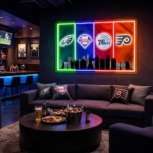 May include: A rectangular neon wall sign featuring four vertical color panels in green, blue, red, and orange. The sign displays the Philadelphia Eagles, Phillies, 76ers, and Flyers logos above a black silhouette of the Philadelphia city skyline.