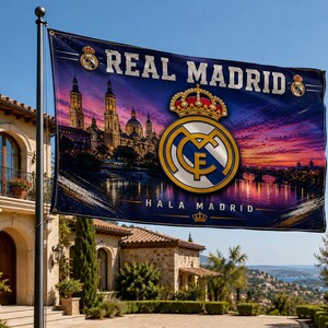 Może przedstawiać: Flaga Realu Madryt z logo drużyny oraz napisami "REAL MADRID" i "HALA MADRID" na tle zachodu słońca. Flaga przedstawia herb z koroną i krajobrazem miejskim.