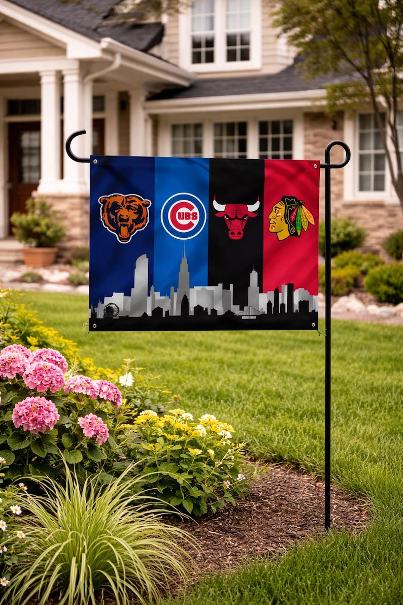 May include: A garden flag displaying the logos of the Chicago Bears, Chicago Cubs, Chicago Bulls, and Chicago Blackhawks. The flag has a black skyline at the bottom. The flag is displayed in a garden with pink flowers.