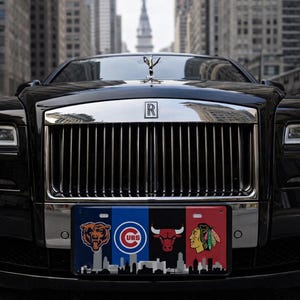 May include: A black Rolls-Royce with a silver grille and hood ornament. The number plate features logos for the Chicago Bears, Cubs, Bulls, and Blackhawks, with a cityscape silhouette. The car is parked on a city street.