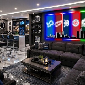 May include: A large rectangular wall art piece featuring five vertical neon-style panels in blue, red, white, red, and green. The panels display sports team logos above a black silhouette of a city skyline, mounted on a dark gray living room wall.